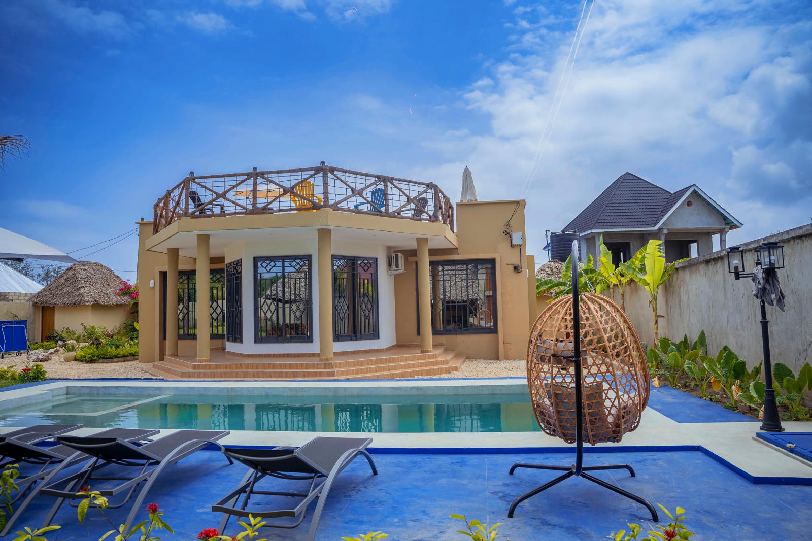 Piscine de la villa avec fauteuil suspendu et transats, jardin de gravier et cocotiers à Zanzibar